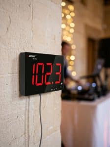 Digital sound level meter showing 95 dB, wall-mounted box used to monitor noise levels at a wedding venue